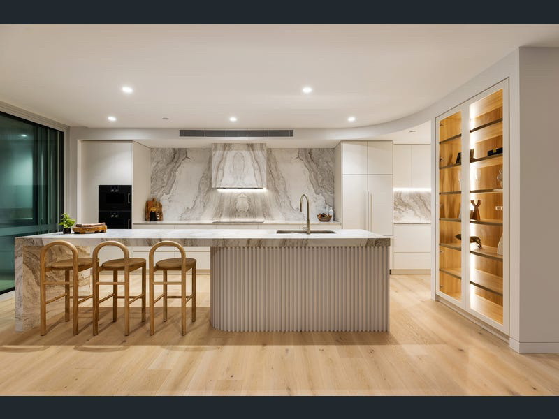 Marble kitchen with fluted island, timber bar stools and lit display joinery