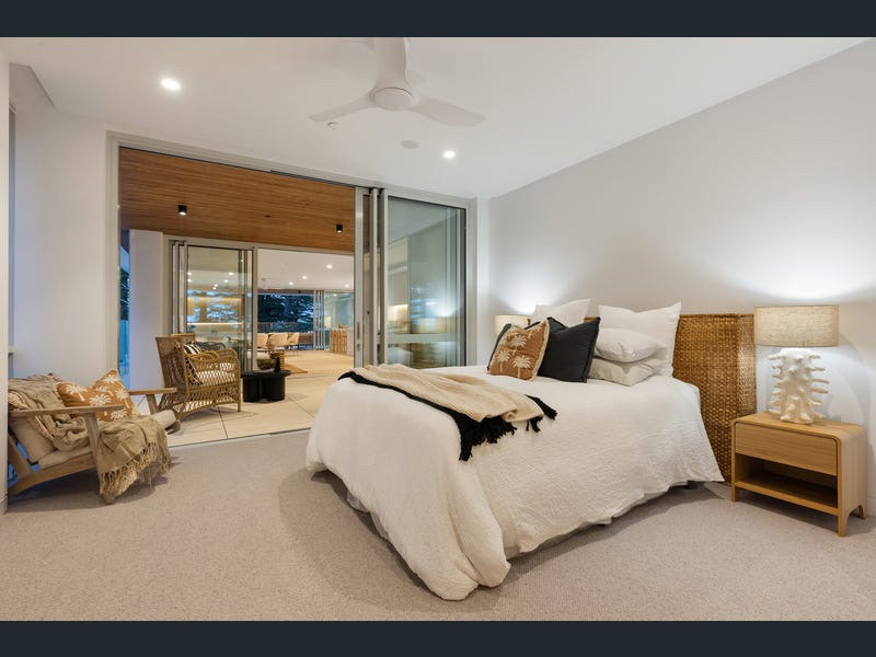 Bedroom styled in white linen and tan tones opening onto the timber-lined terrace
