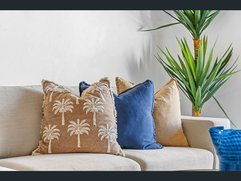 Styling detail — palm-embroidered and blue linen cushions on a linen sofa